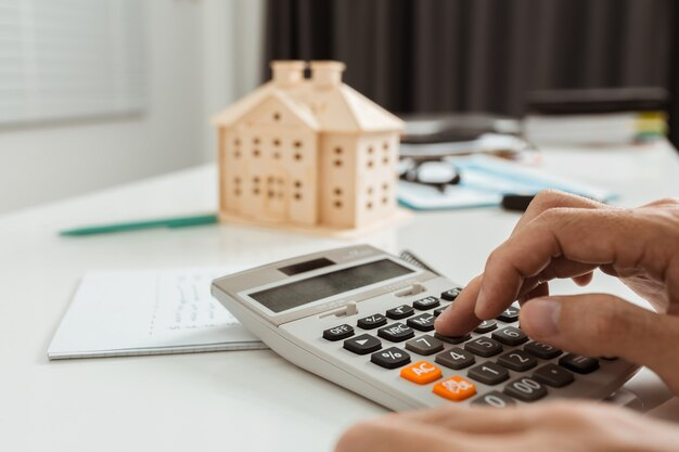 Hand using Calculator and Miniature House on Table